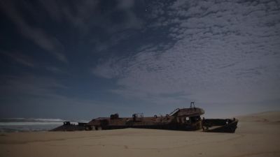 Along the coast, a shipwreck has been swallowed by the sand. - Earth at Night in Color