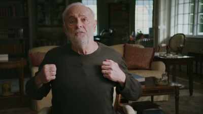 He's stretching his chest.
He's opening his shirt. - George Carlin's American Dream