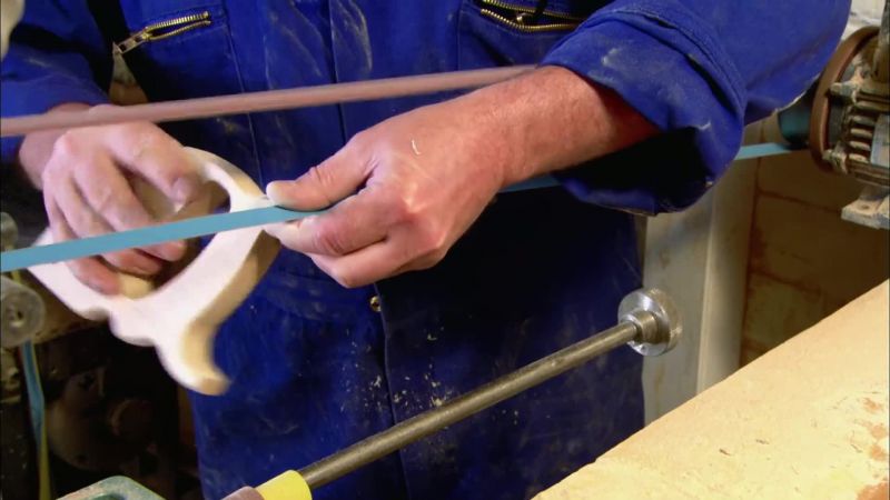 He sands the edges of the handle until it's smooth