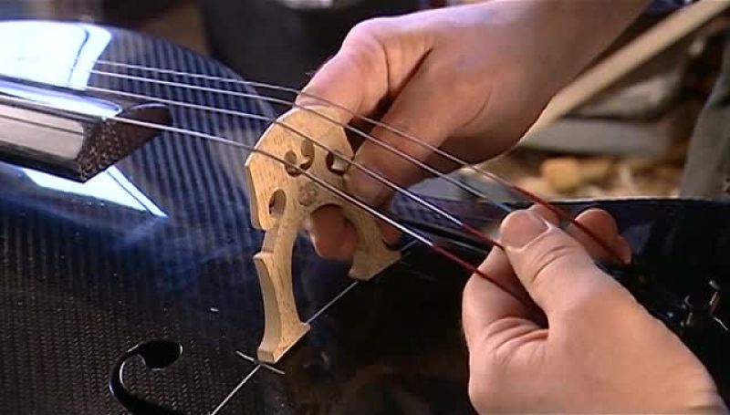NOW HE SLIDES THE STRINGS INTO THE GROOVES ON THE BRIDGE