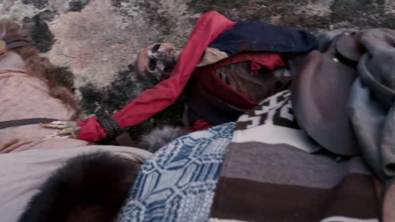 That's where the corpse strapped to his back comes in