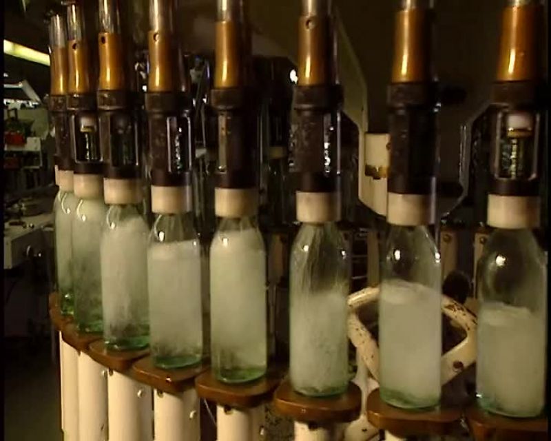 THE NEXT STEP, A CAPPER PLACES CAPS ON THE BOTTLES